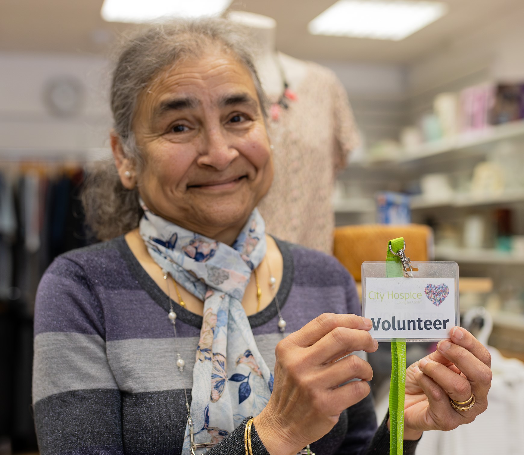 A City Hospice charity shop volunteer proudly holds her volunteer lanyard