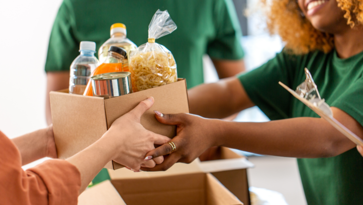 A food bank volunteer in a green T-shirt gives someone a box of food