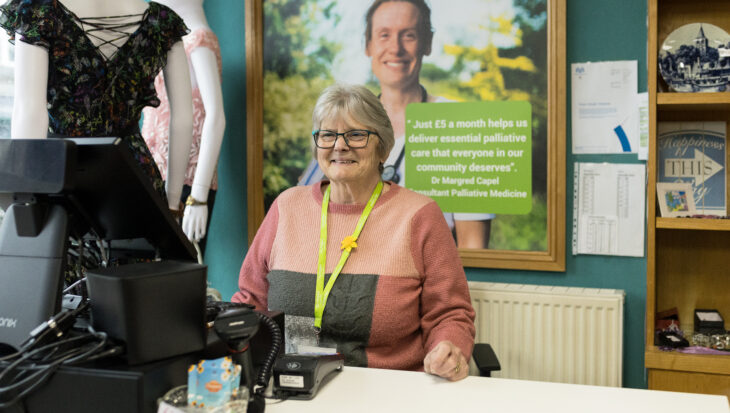 A volunter welcomes customers behind the counter of a City Hospice charity shop
