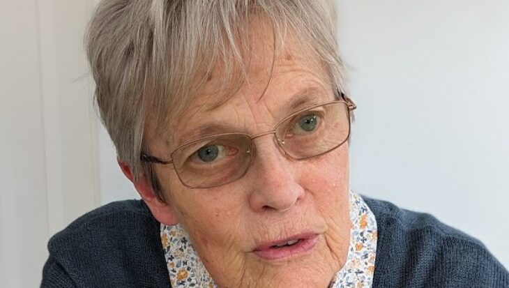 Jan with short grey hair, wearing glasses, a floral shirt and a navy jumper